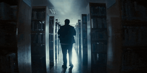 a man is walking through a library with a light shining through the shelves