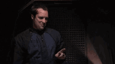 a man in a suit and tie is giving the middle finger while standing in a dark room .