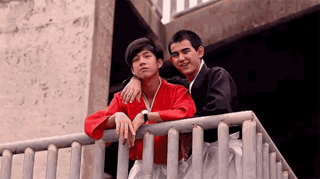 two young men are standing next to each other on a railing .