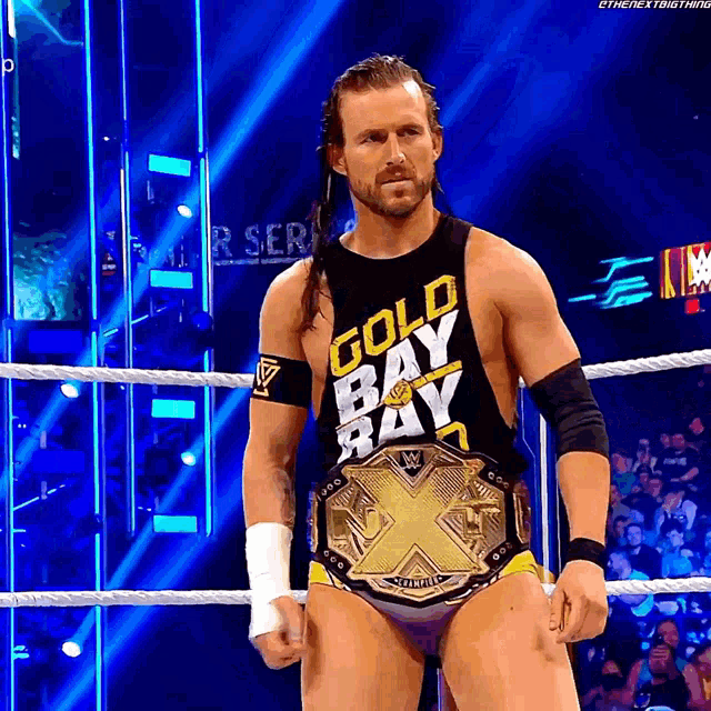 a wrestler wearing a gold bay bay shirt stands in a wrestling ring