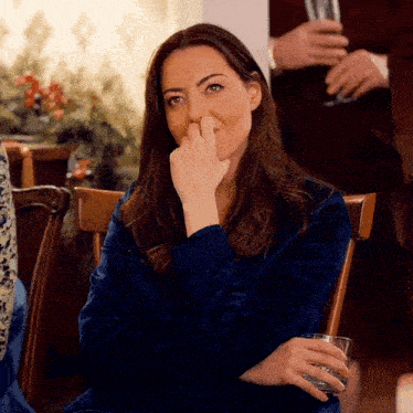 a woman is sitting in a chair with her hand on her nose and holding a glass of wine .