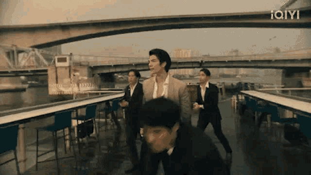 a group of men in suits are dancing in front of a bridge .