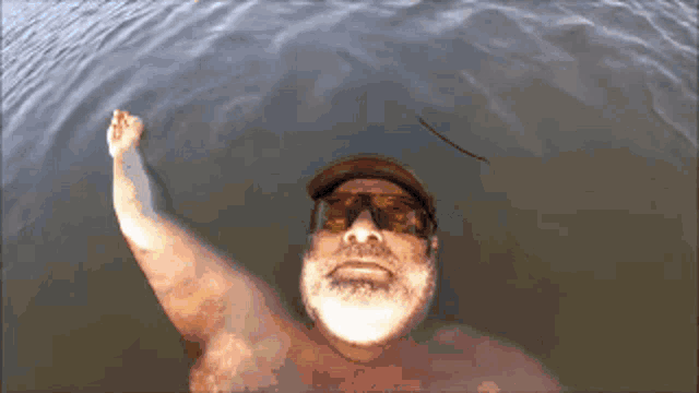 a man with a beard and sunglasses is swimming in a body of water