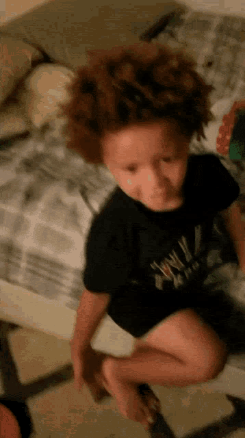 a young boy is sitting on a bed wearing a black shirt that says ' tony '