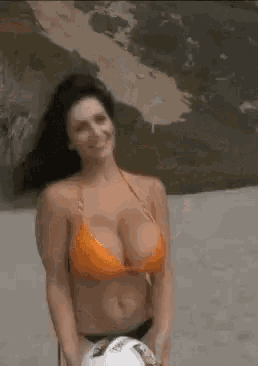 a woman in an orange bikini is standing on a beach holding a volleyball .