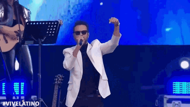 a man in a white jacket singing into a microphone with #vivelatino written in the corner