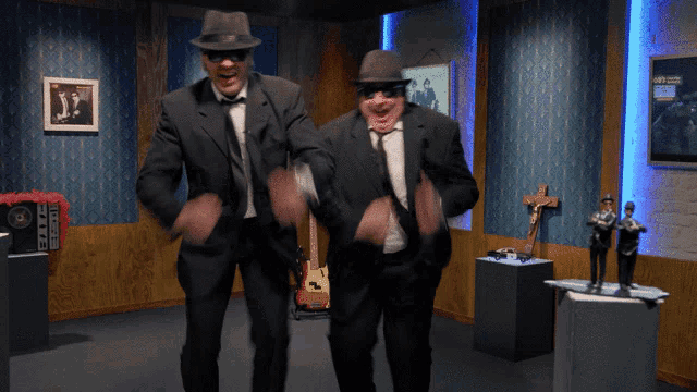two men in suits and hats are dancing in a room with a sign that says casio on it