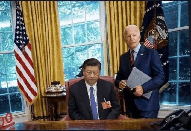 a man in a suit and tie is sitting at a desk next to a man in a suit and tie holding a folder .