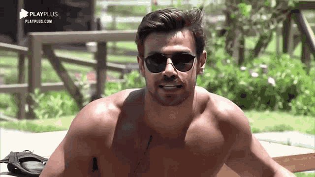 a shirtless man wearing sunglasses is sitting on a wooden bench .