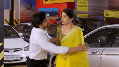 a woman in a yellow saree is being hugged by a man in a white shirt
