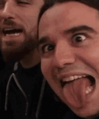a man with a beard is sticking his tongue out while another man looks on .