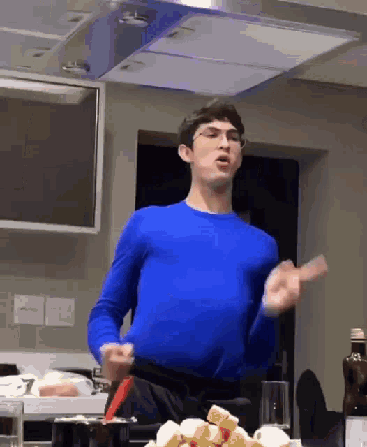 a man in a blue sweater is standing in front of a table full of food