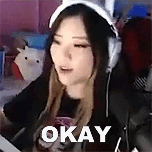 a woman wearing headphones is sitting in front of a computer and says `` okay '' .