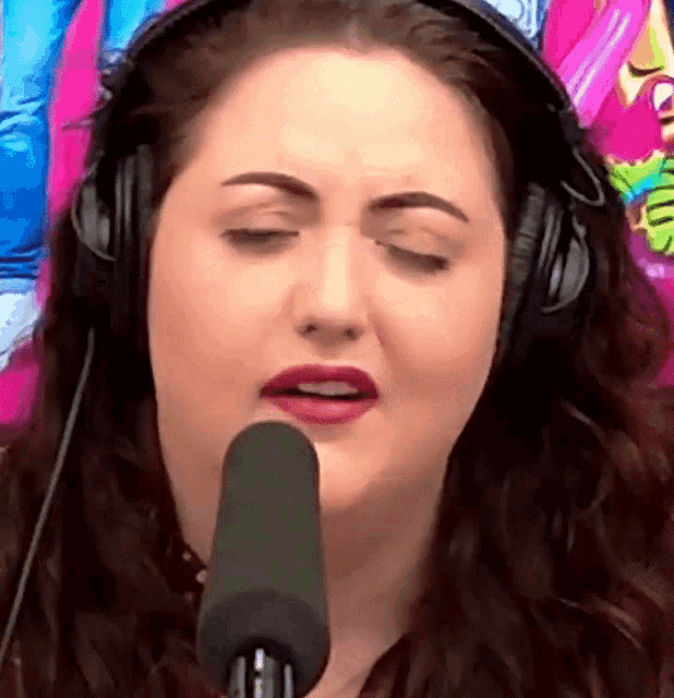 a woman wearing headphones singing into a microphone with her eyes closed