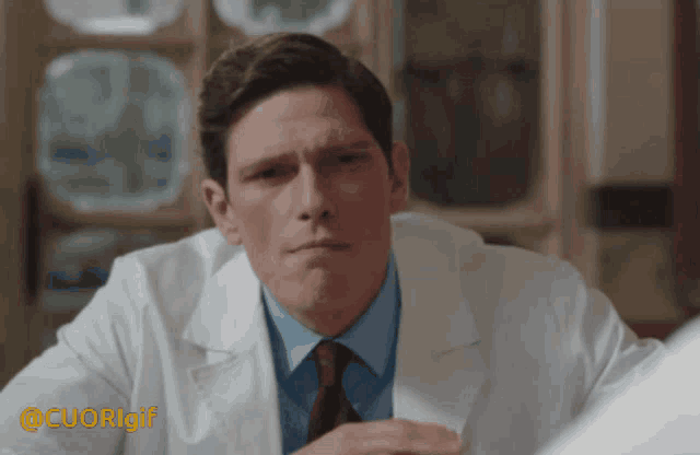 a man in a lab coat and tie is sitting at a table