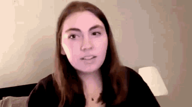 a young woman is sitting on a bed talking to a camera .