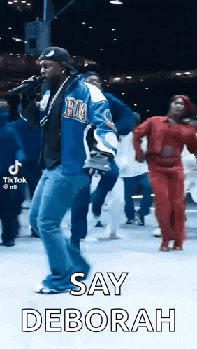 a man is singing into a microphone while a group of people are dancing behind him .