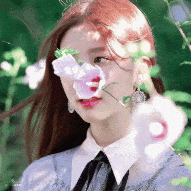 a woman is holding a flower in front of her nose .