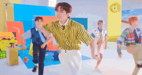 a group of young men are dancing together in a room with a clock in the background .
