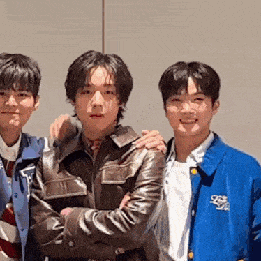 three young men are posing for a picture together . one of the men is wearing a blue jacket .