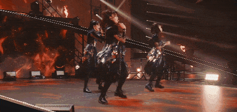 a group of women are dancing on a stage in front of a fire