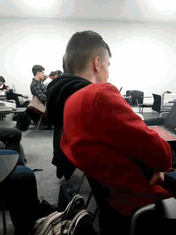 a man in a red sweatshirt sits in a classroom