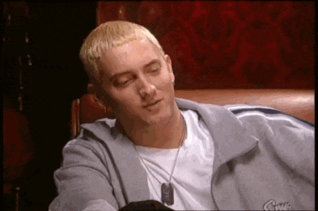 eminem is sitting on a couch with his eyes closed and wearing a gray jacket .