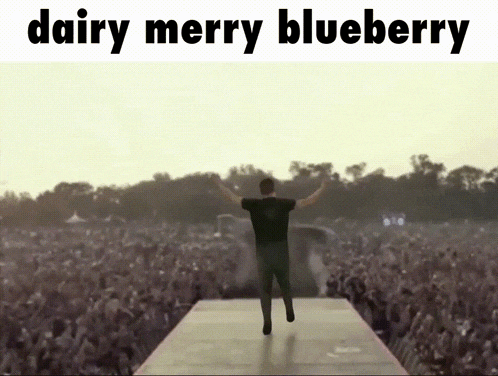 a man stands on a stage in front of a crowd with the words " dairy merry blueberry " above him