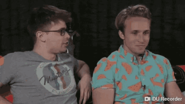 two men are sitting next to each other in a room and one of them is wearing a watermelon shirt .