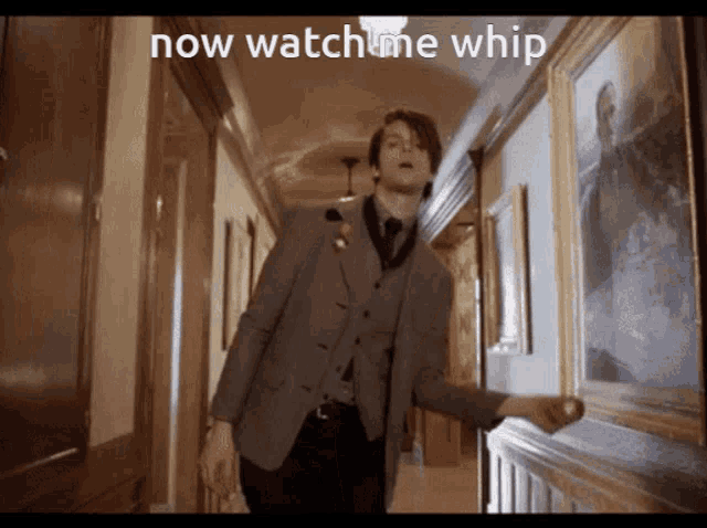 a man in a suit and tie is standing in a hallway with the words now watch me whip below him