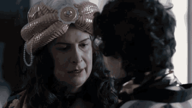 a woman wearing a turban and pearls is talking to a young boy .