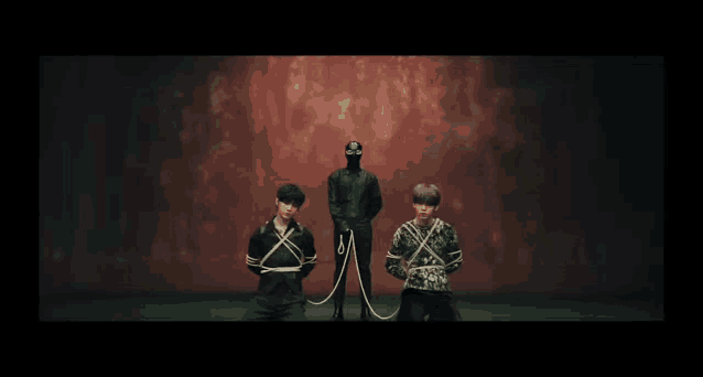 a man in a mask is standing behind two men tied up with ropes