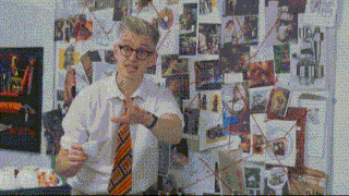a man wearing glasses and a tie is standing in front of a wall with pictures on it .