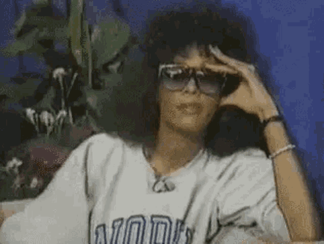 a woman wearing sunglasses and a t-shirt is sitting on a bed .
