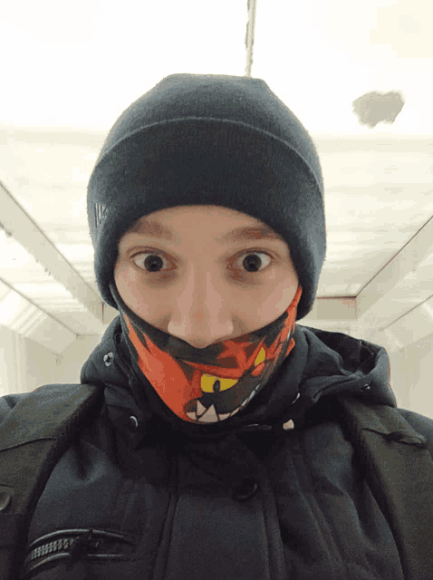 a person wearing a beanie and a scarf around their neck has a surprised look on their face