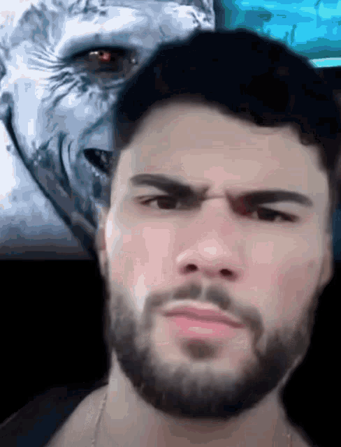 a man with a beard is making a funny face in front of a picture of a monster 's face .