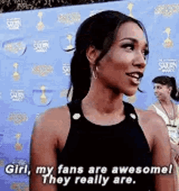 a woman is standing in front of a blue wall and saying `` girl , my fans are awesome ! they really are . ``
