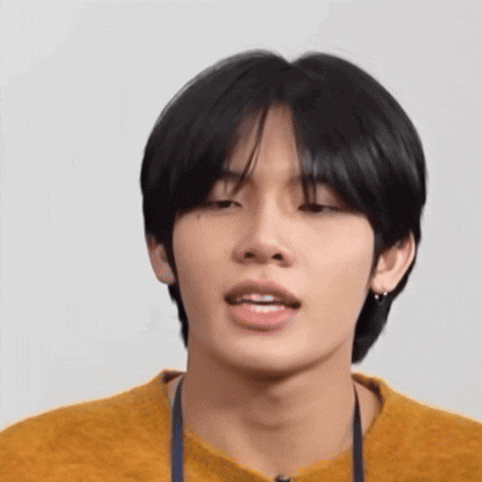 a close up of a young man 's face wearing a yellow sweater and earrings .