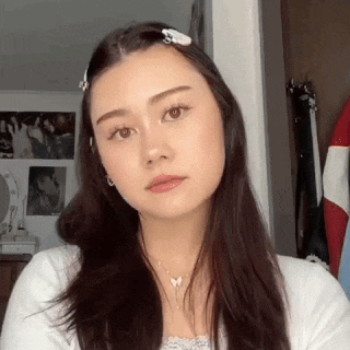 a woman with long dark hair is wearing a white shirt and a butterfly necklace .