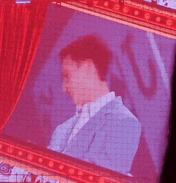 a man in a suit is behind a red curtain on a large screen