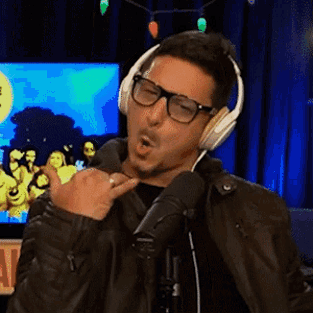 a man wearing headphones and glasses is giving a thumbs up sign while standing in front of a microphone .
