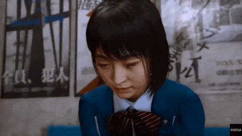 a girl in a school uniform and tie is sitting in front of a wall with posters on it .