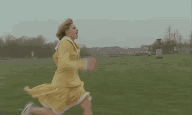 a woman in a yellow dress is running through a grassy field .