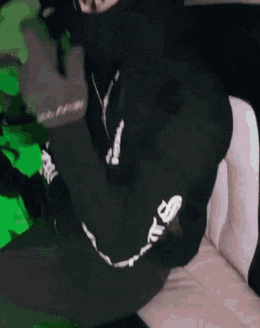 a person wearing a black mask and a green hoodie is sitting on a chair .