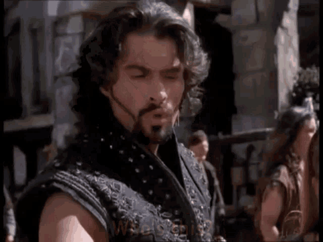 a man with a beard and long hair is wearing a black vest with studs on it .