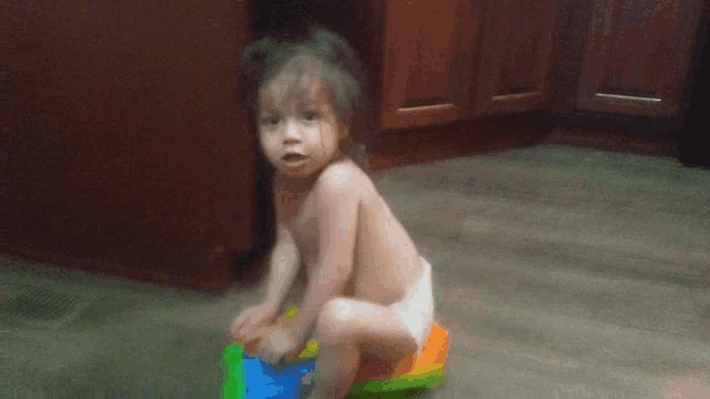 a baby in a diaper sits on a toy on the floor