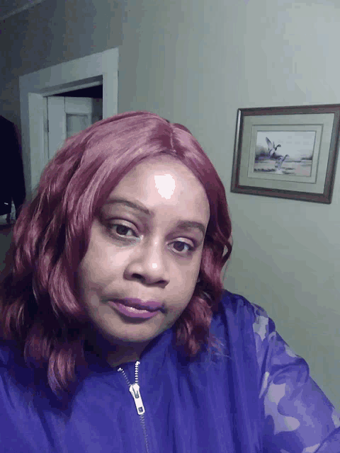 a woman with red hair is wearing a purple jacket in front of a framed picture