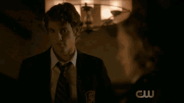 a man in a suit and tie stands in front of a chandelier with the letters cw on it