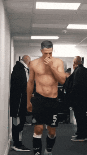 a shirtless soccer player with the number 45 on his shorts walks down a hallway