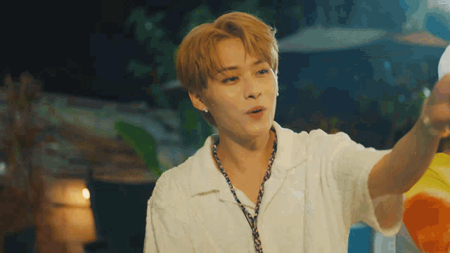 a young man wearing a white shirt and a necklace is holding a bottle